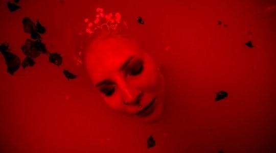 Fotografi av Pernille Azoras ansikt som dukker opp av rødfarget vann