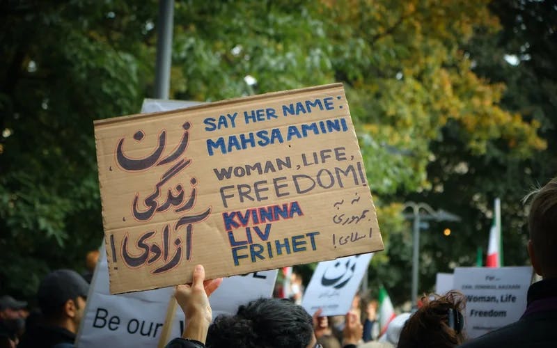 Fotografi av protestplakat med teksten "Kvinne, liv, frihet" og "Say her name: Mahsa Amini"